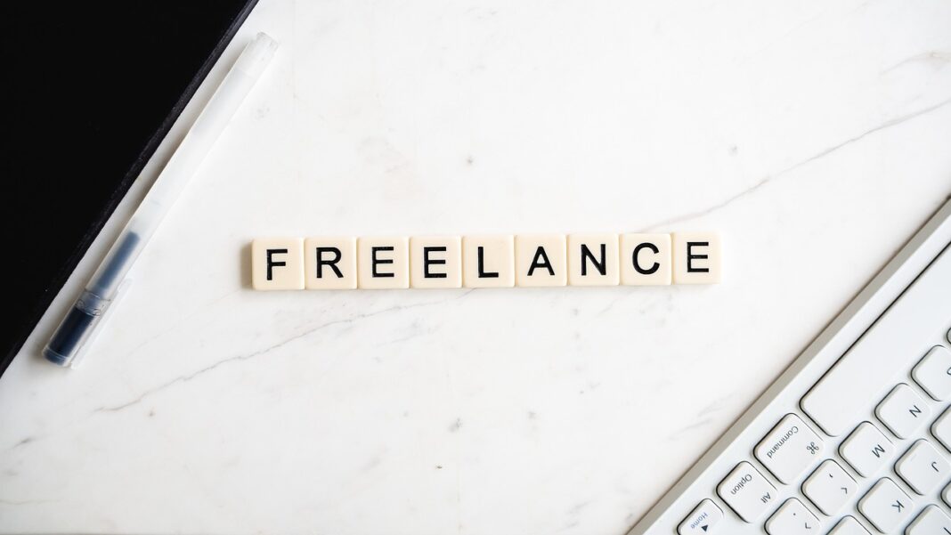 LBV-021 Das Wort „FREELANCE“ aus Buchstabenplättchen auf einer weißen Marmoroberfläche, daneben ein weißer Stift und ein Teil einer Computertastatur.