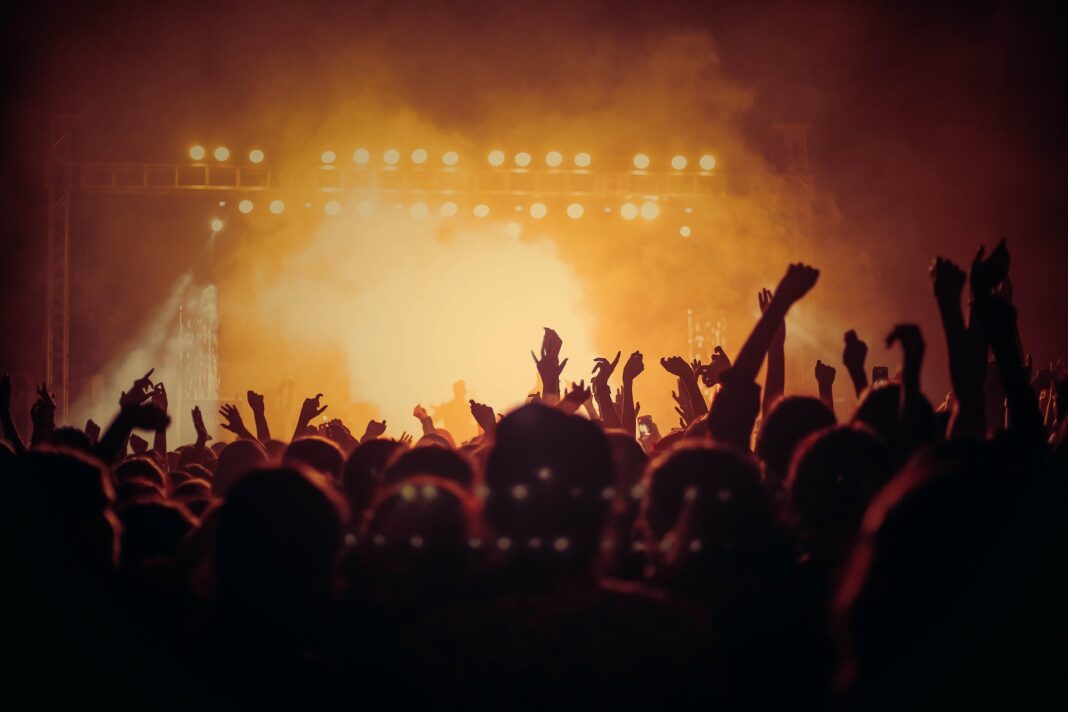 Menschenmenge bei einem Konzert, mit erhobenen Händen, während intensive Lichter und Nebel die Szene erleuchten.