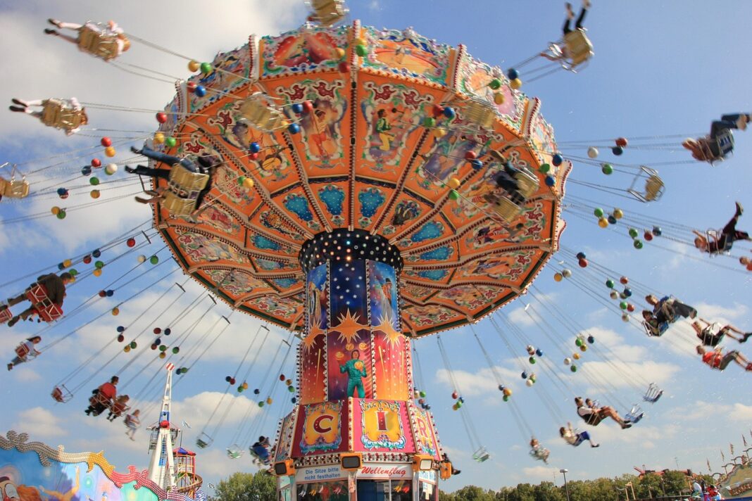 Kettenkarussell auf einem Jahrmarkt mit Menschen in den schwebenden Sitzen vor blauem Himmel.