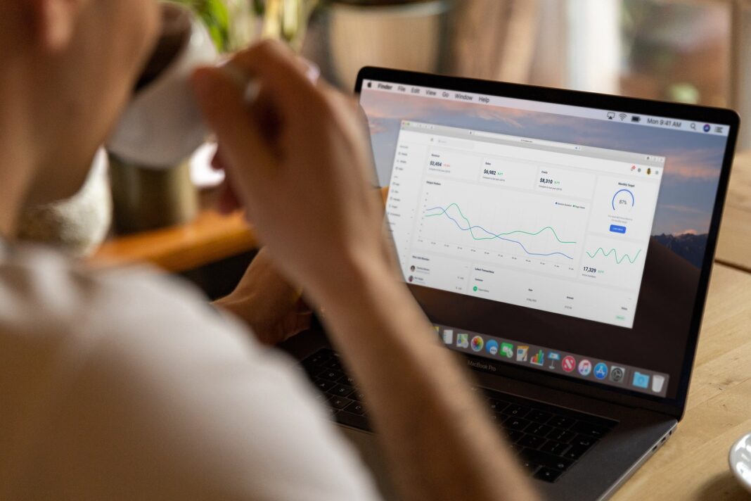 Person trinkt Kaffee und betrachtet ein Dashboard mit Diagrammen und Statistiken auf einem Laptop-Bildschirm.