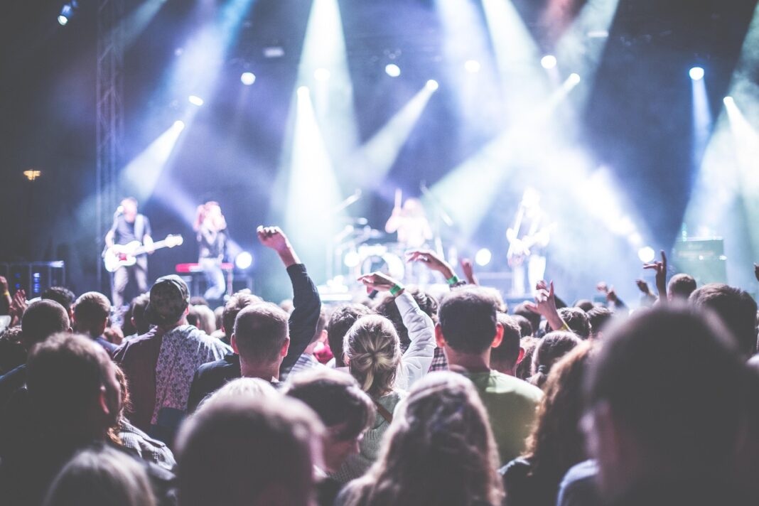 Publikum bei einem Live-Konzert, das begeistert vor einer beleuchteten Bühne steht, auf der eine Band auftritt.