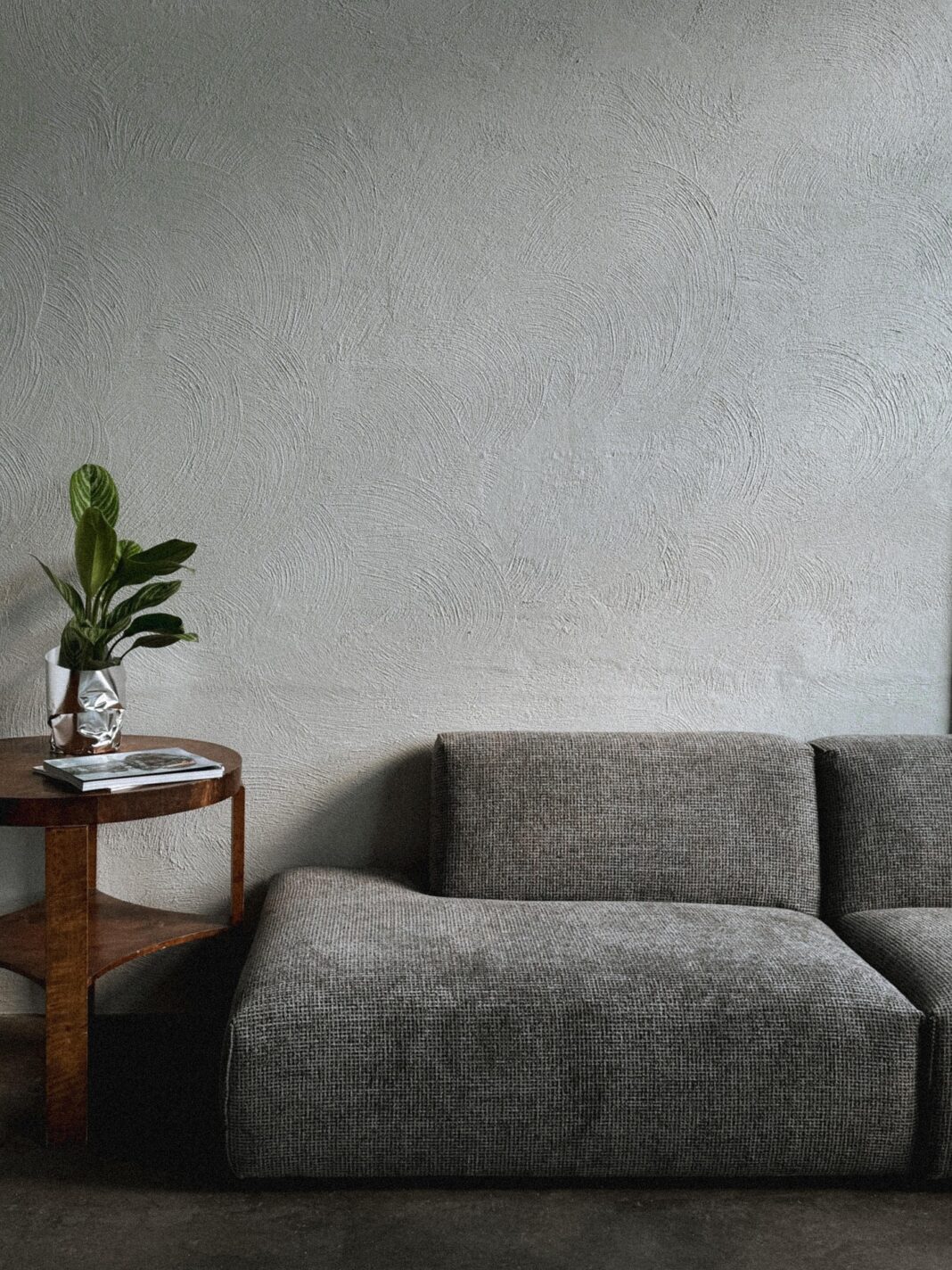 Ein modernes Wohnzimmer mit einem grauen Sofa, einem kleinen Holztisch und einer Pflanze in einer silbernen Vase.