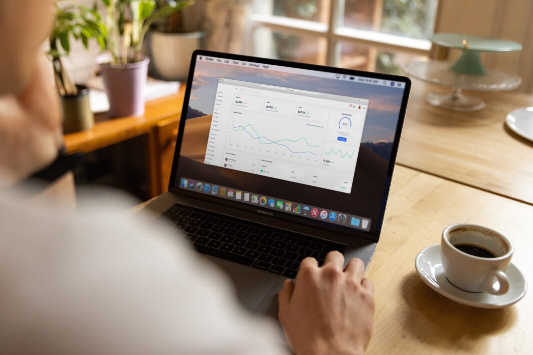 Person arbeitet an einem MacBook mit geöffneter Analyse-Software in einem gemütlichen Raum mit Kaffeetasse auf dem Tisch