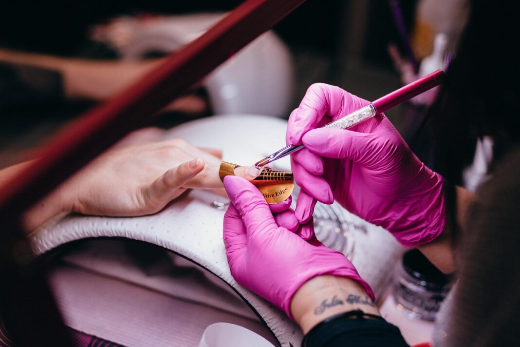 Nageldesign-Profi arbeitet mit Schablone und Pinsel an künstlicher Fingernagelverlängerung