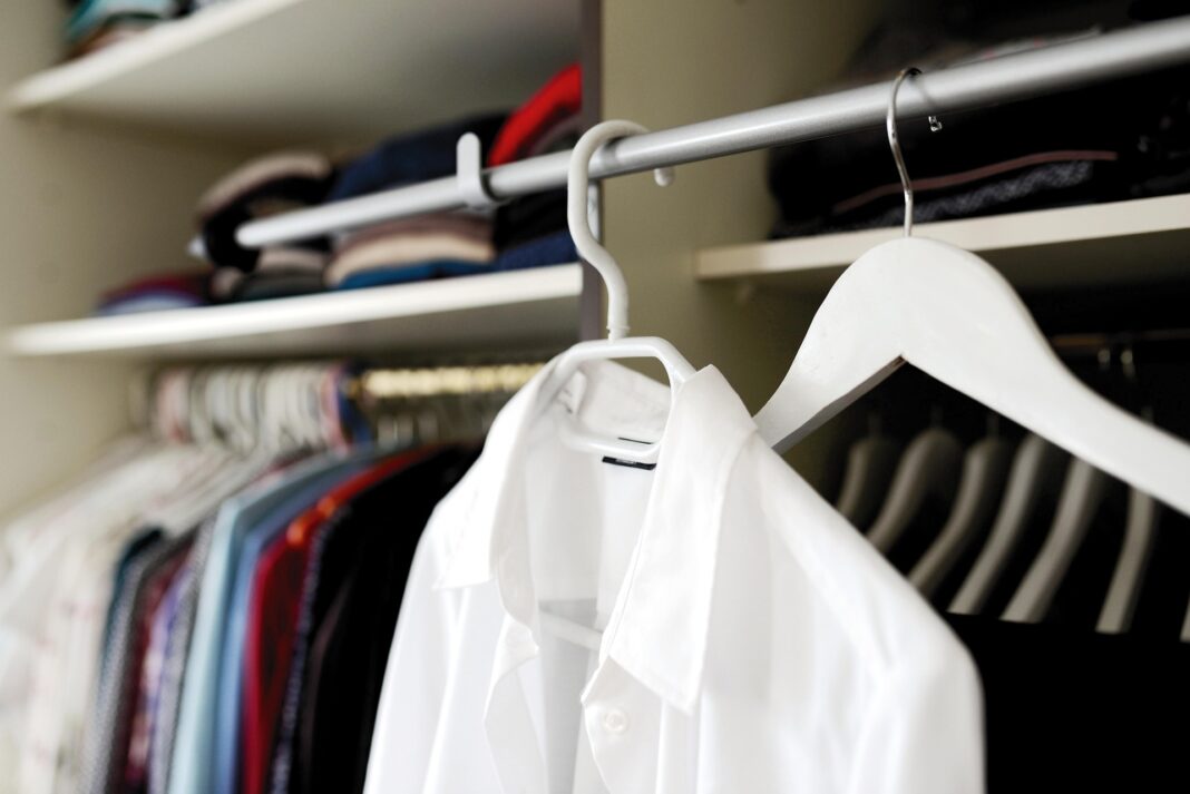 Weiße Bluse auf Kleiderbügel in einem ordentlich sortierten Kleiderschrank.